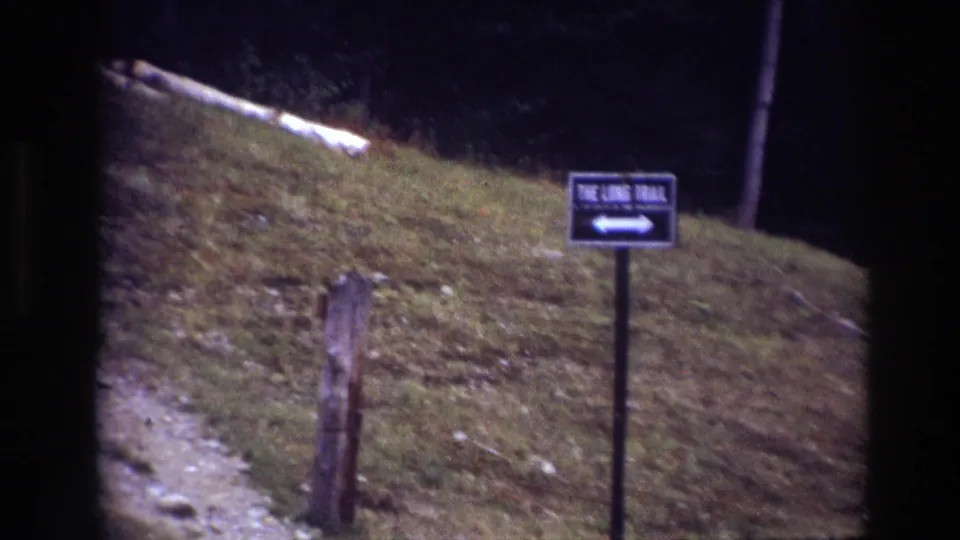 1967 Ottawa park frame showing a trail sign on a grassy slope with a path edge and wooded background.