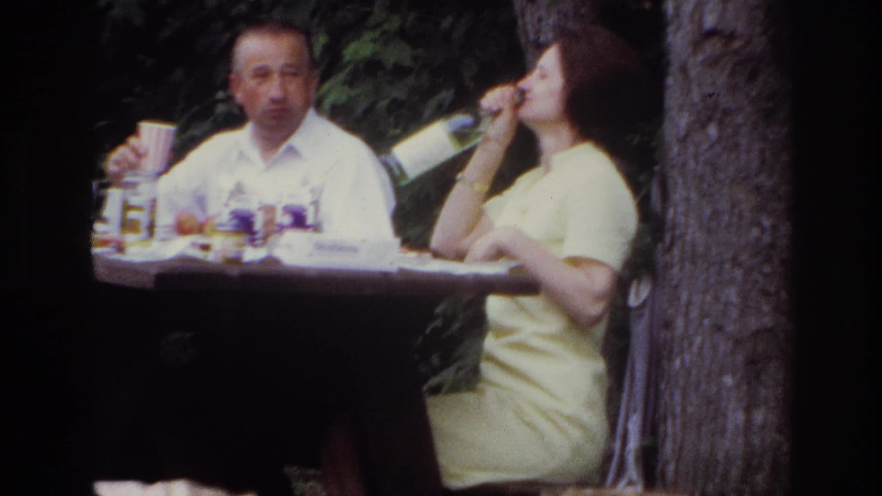 Man holding a cup beside a woman in yellow drinking from a bottle at a picnic table.