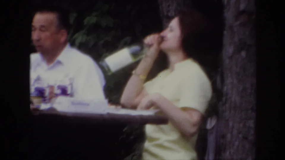 Soft 8mm close view from the Ottawa picnic, with a woman in a yellow dress drinking from a bottle near a seated man.