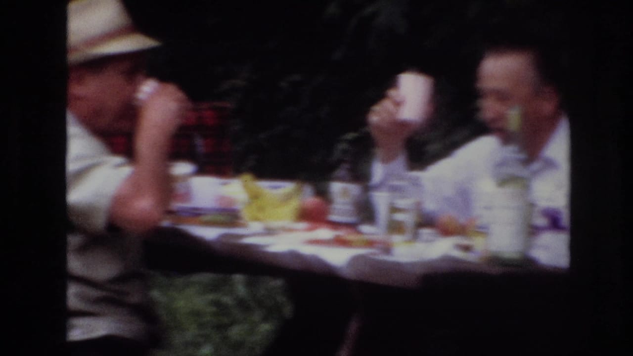 1967 Ottawa picnic scene with a man in a straw hat drinking from a cup at a table, with another seated adult and food visible.