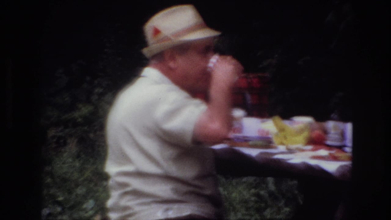 Side view from 1967 Ottawa home-movie footage showing a man in a straw hat drinking at a picnic table with fruit and tableware.