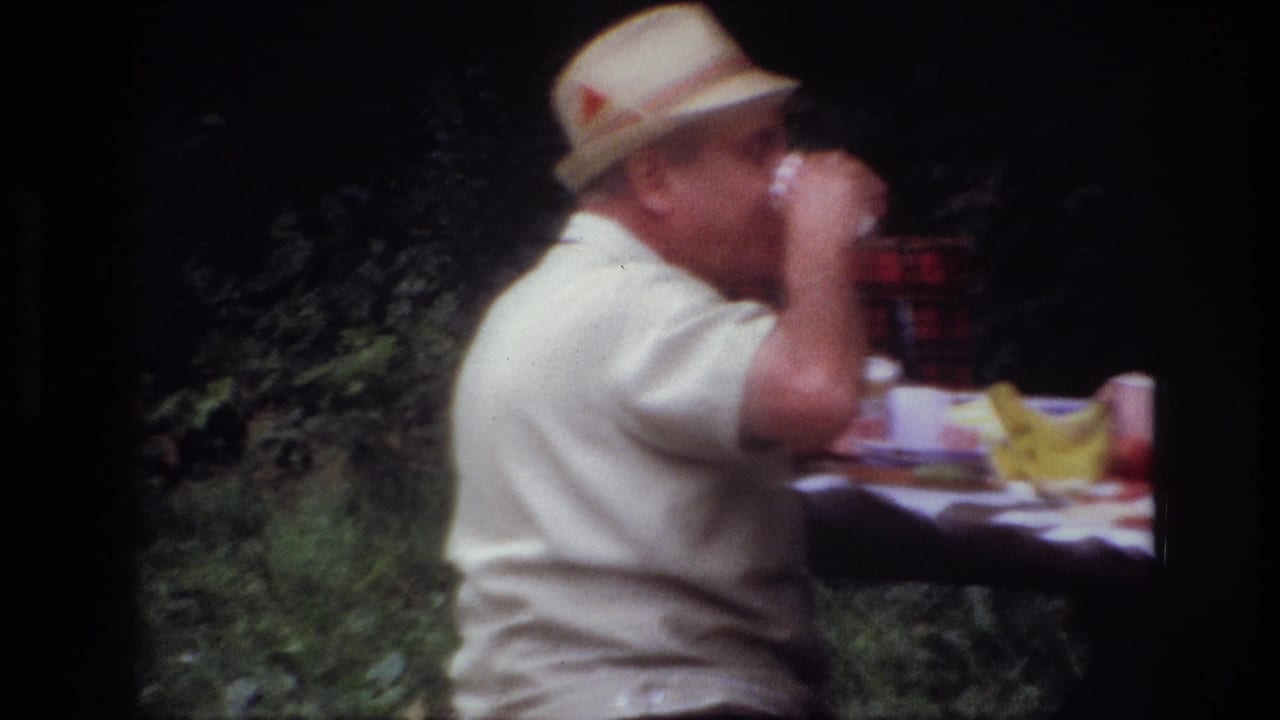 1967 Ottawa frame of a seated man in a straw hat drinking from a cup, with picnic food and foliage in the background.