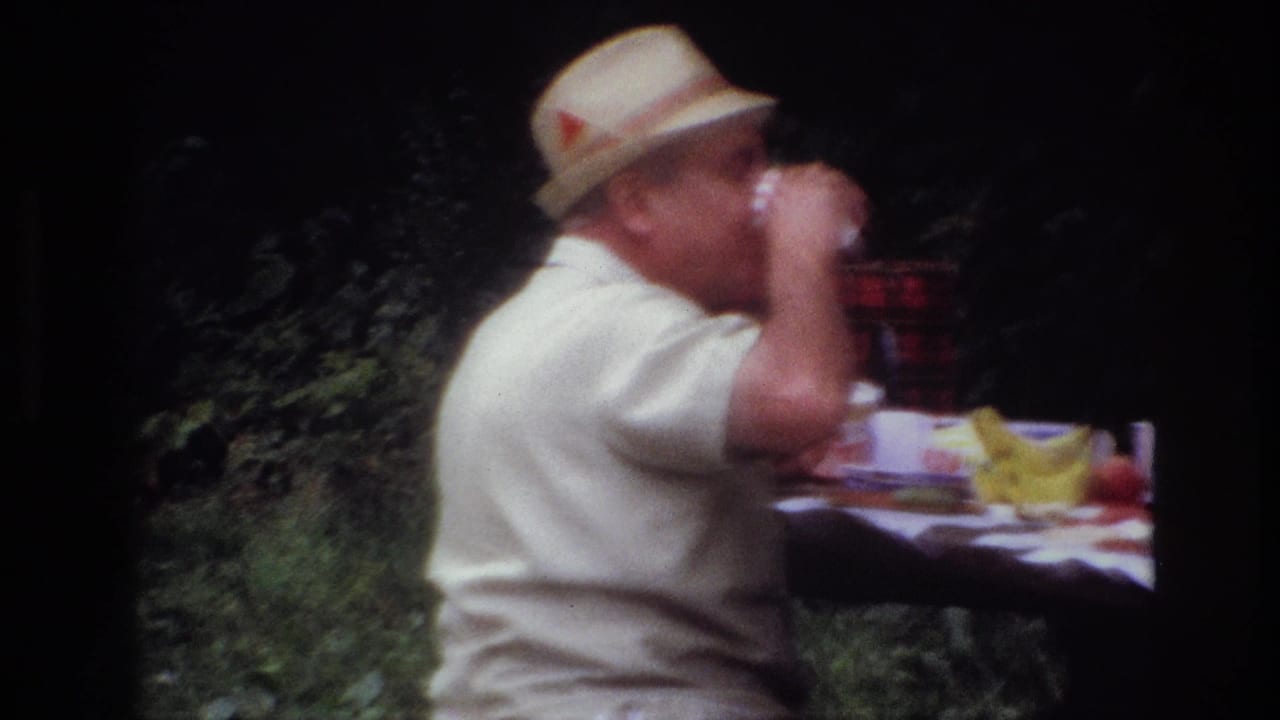 In Ottawa home-movie footage from 1967, a man in a light shirt and straw hat drinks at a picnic table under trees.