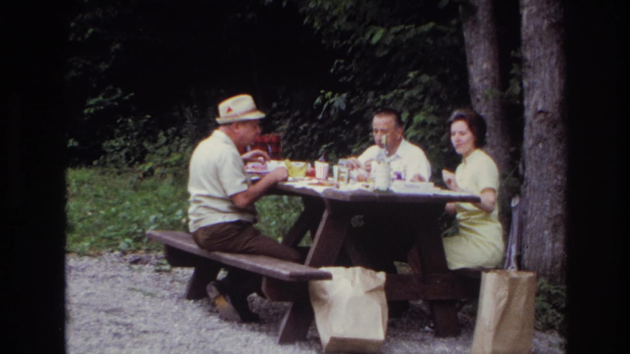 Ottawa 1967 home-movie frame showing three adults eating at a wooden picnic table in a forested park setting.