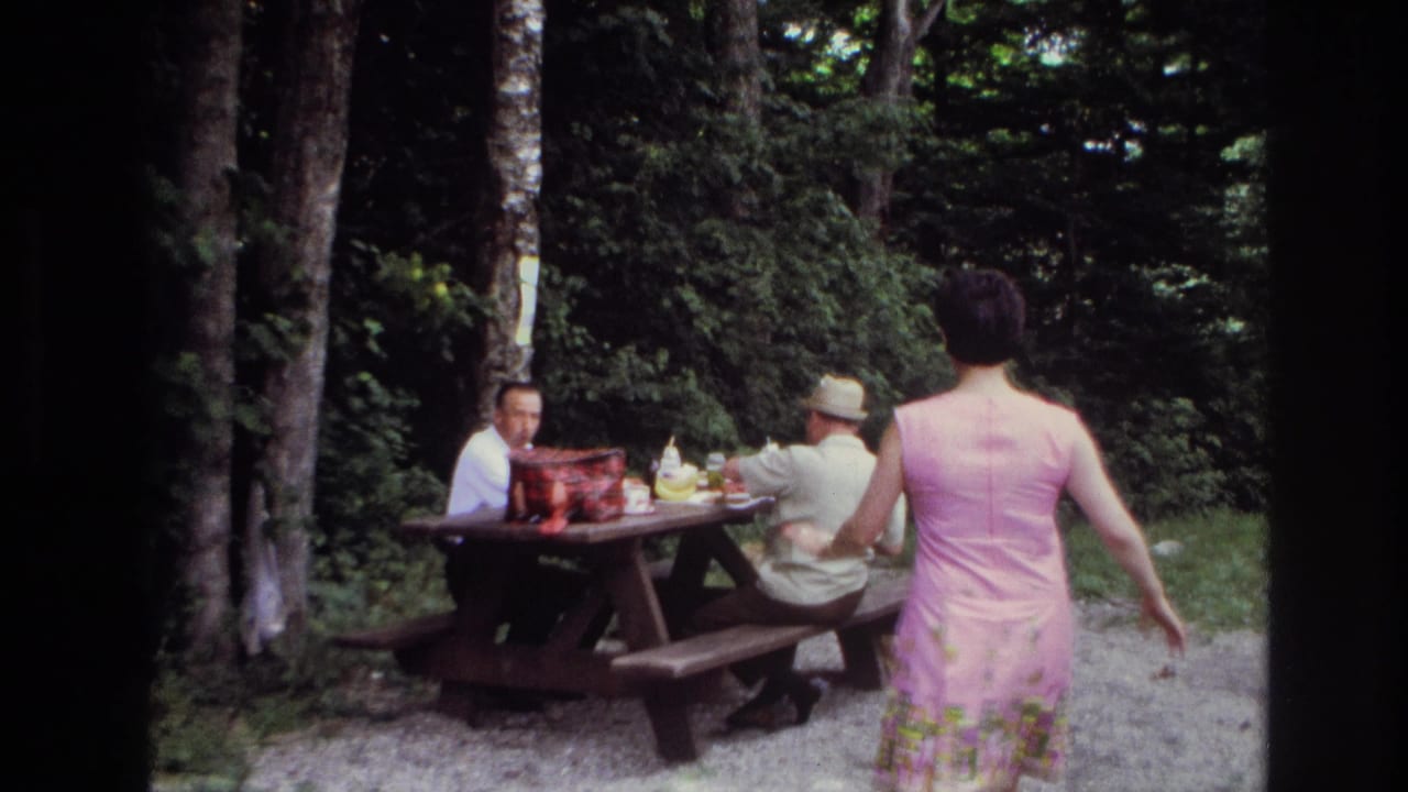 In supported 1967 Ottawa home-movie footage, a woman in a pink dress approaches two men at a picnic table in a forested campground.