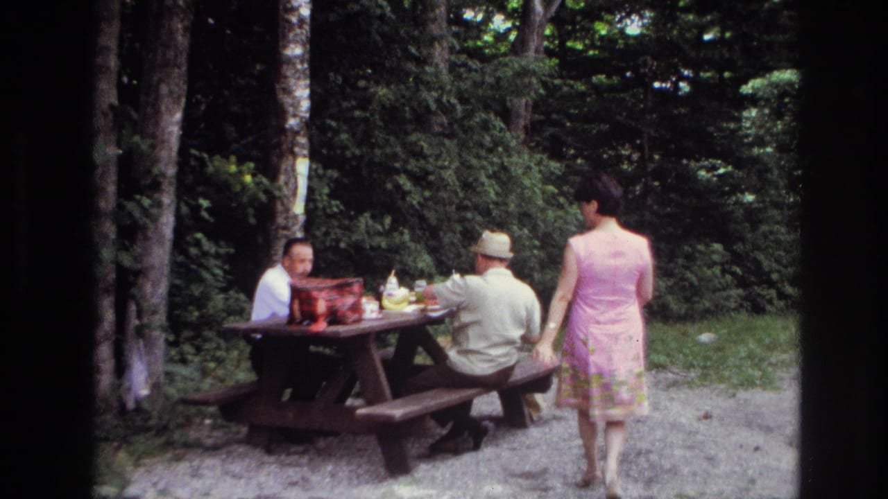 Woman stands near a picnic bench while two men remain seated at the table.