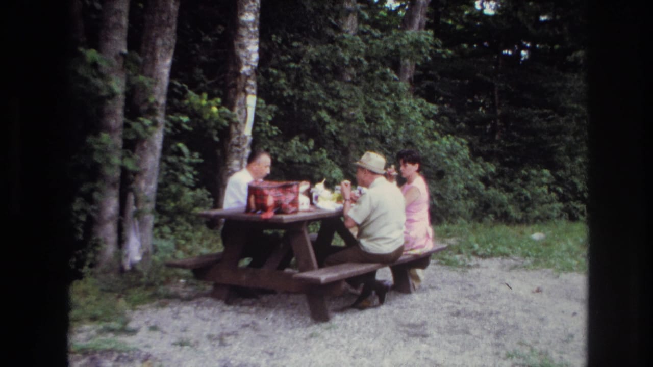 In 1967 Ottawa home-movie footage, three adults appear to eat at a wooden picnic table beside trees and dense green foliage.