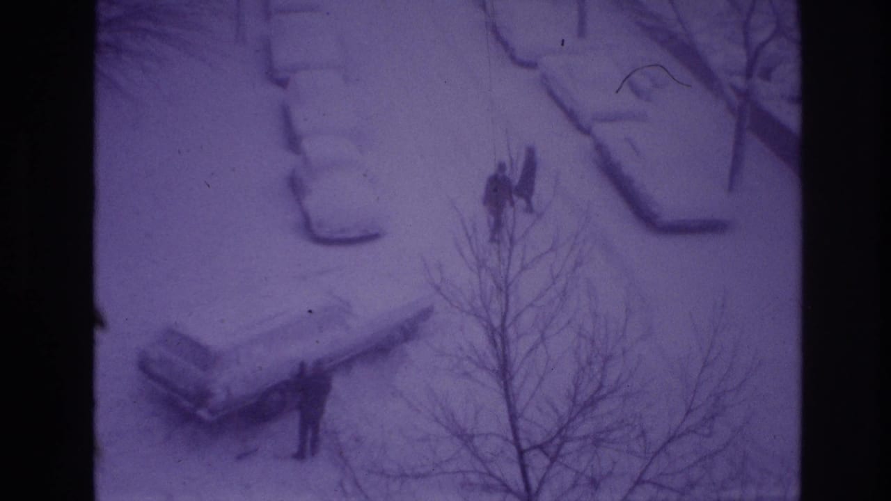 High-angle 1967 Ottawa home-movie frame showing people walking along a snowy street with cars buried in snow and bare tree branches in front.