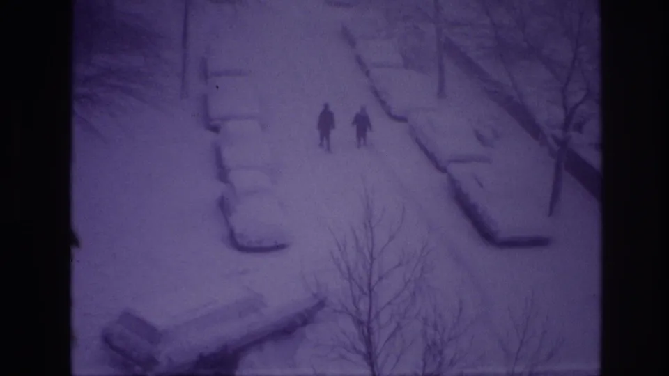 High-angle 1967 Ottawa winter view with two distant people walking past snow-covered cars and bare roadside trees.
