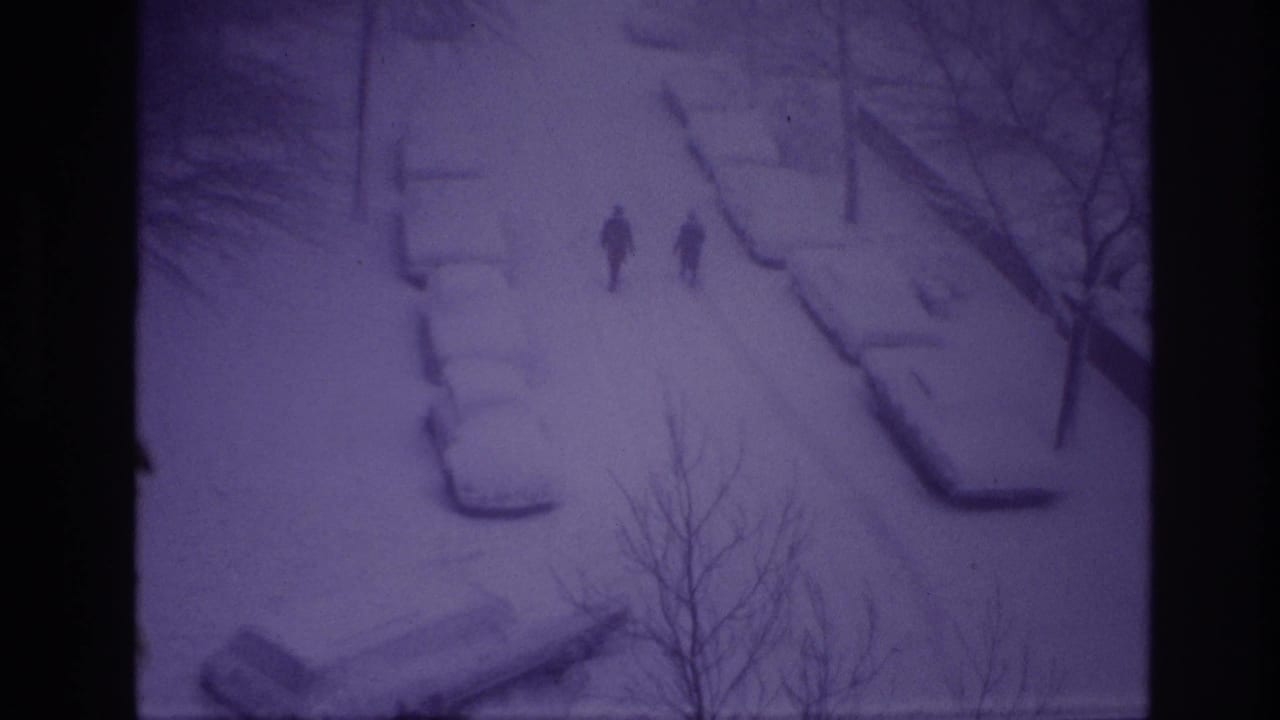 1967 Ottawa 8mm frame with two distant pedestrians on a white, snow-filled street beside buried cars and leafless trees.