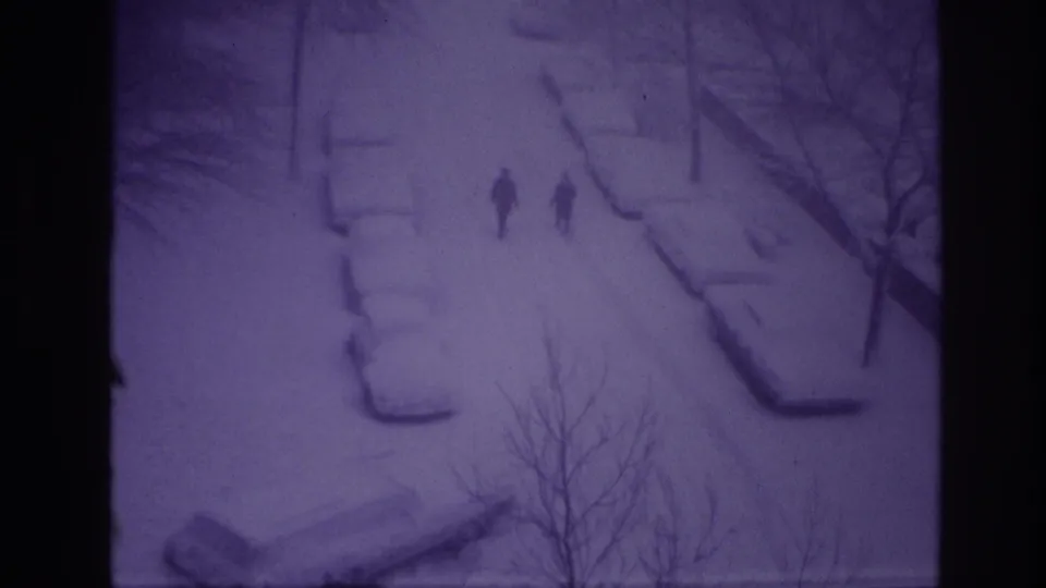 1967 Ottawa 8mm frame with two distant pedestrians on a white, snow-filled street beside buried cars and leafless trees.