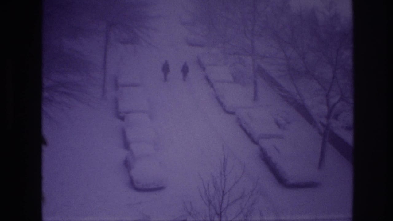 1967 Ottawa home-movie frame with two men walking down a snowy street lined by bare trees and parked cars.