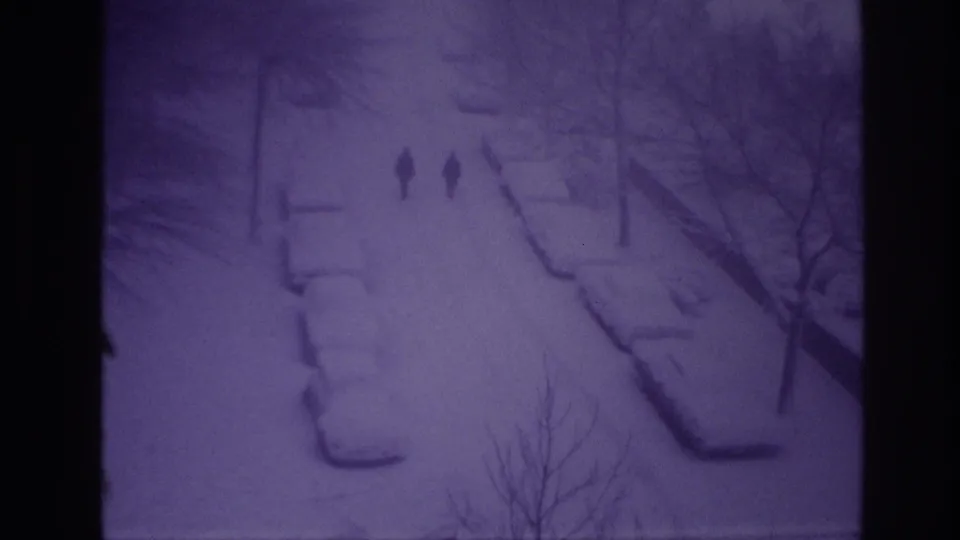 1967 Ottawa home-movie frame with two men walking down a snowy street lined by bare trees and parked cars.