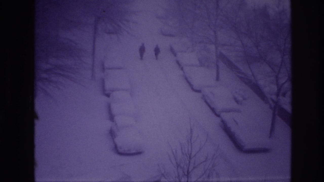 Two figures continue along the snowy street near parked cars and bare trees.