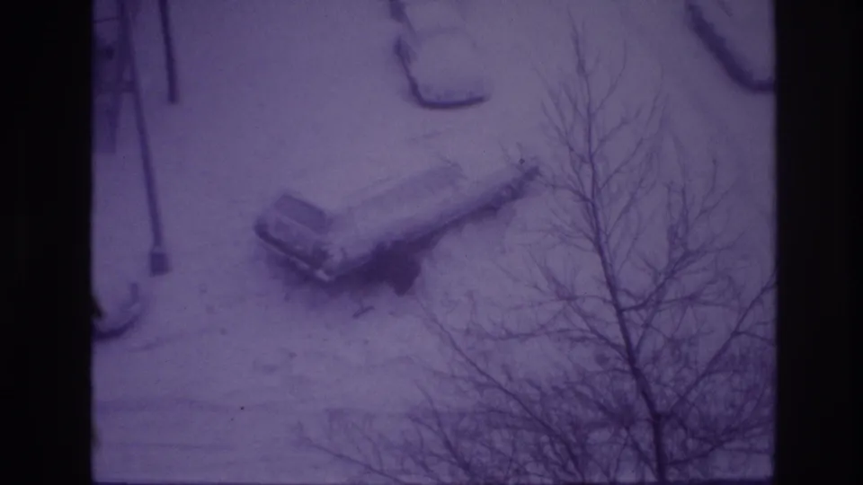 1967 Ottawa winter street frame with a snow-covered parked car, streetlamp, and bare trees in a purple-tinted 8mm view.