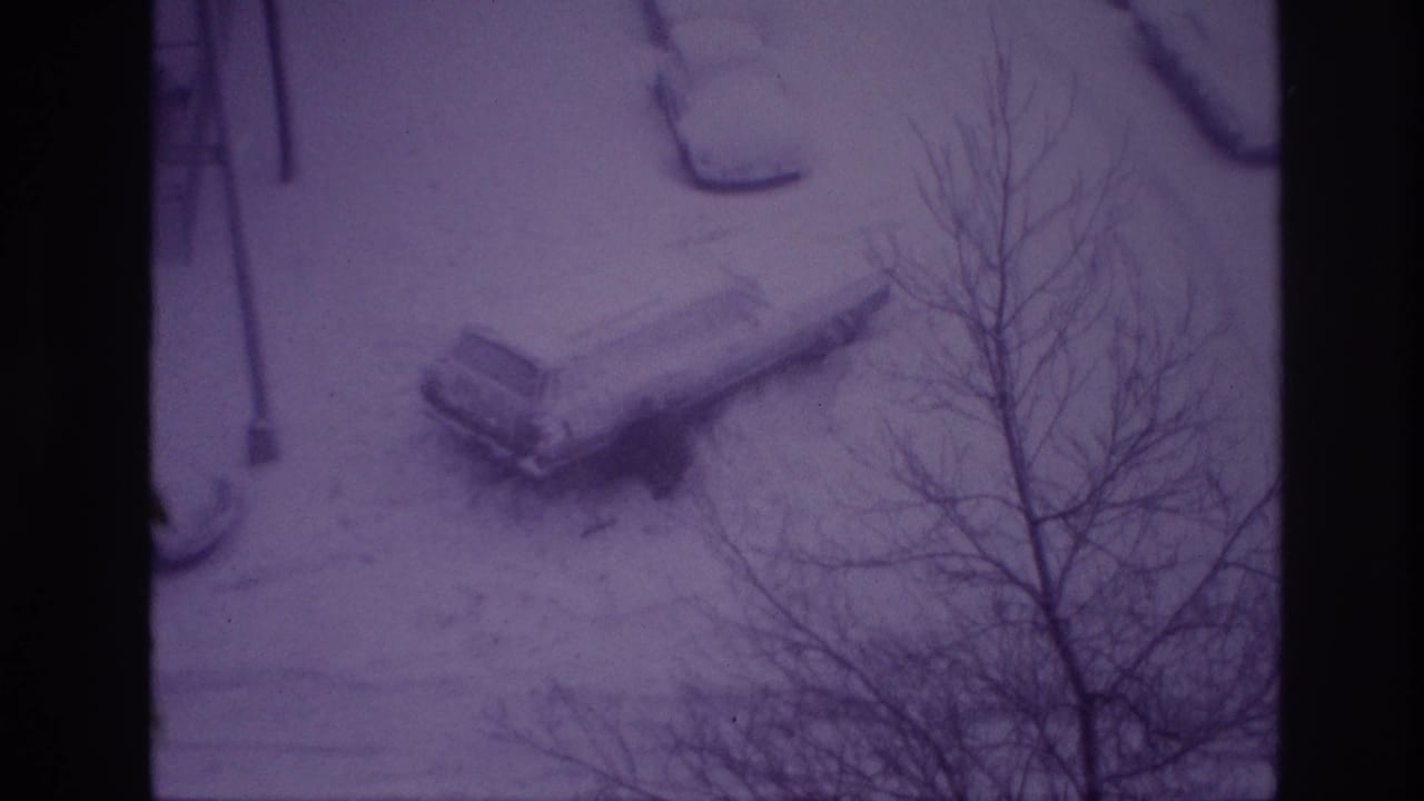High-angle 1967 Ottawa home-movie frame of a snow-covered parked car and winter-bare trees along a residential street.