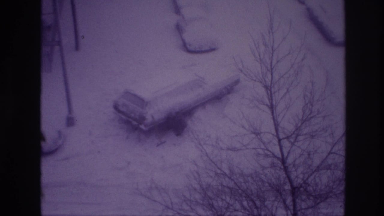 Elevated 1967 Ottawa home-movie view of a parked car buried in snow, with bare branches crossing the frame.