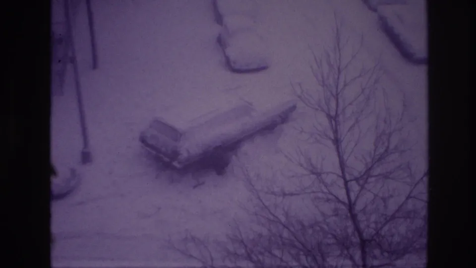 Elevated winter view in Ottawa, 1967, showing a snow-covered parked car near bare branches and a snow-blanketed street edge.