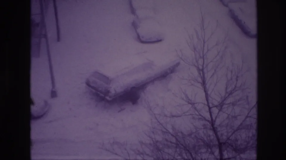 1967 Ottawa home-movie frame with a snow-buried car seen from above through bare winter branches.