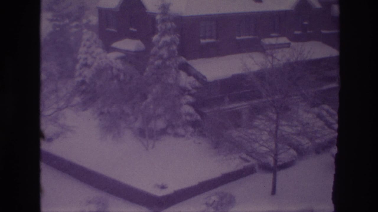 1967 Ottawa home-movie frame of a snowy residential yard, brick house, evergreen trees, parked cars, and walkways.
