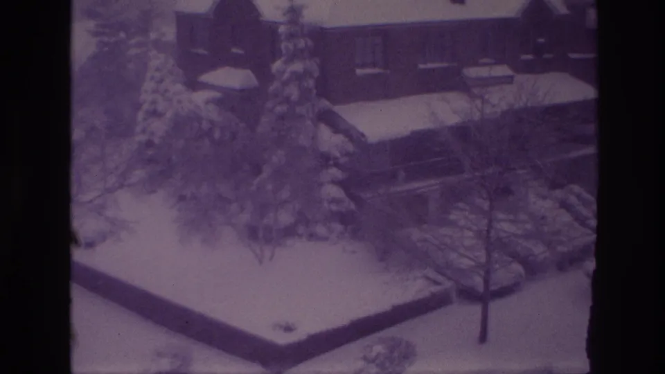 1967 Ottawa winter frame showing a brick residential building, snow-covered trees, parked cars, and a quiet yard.