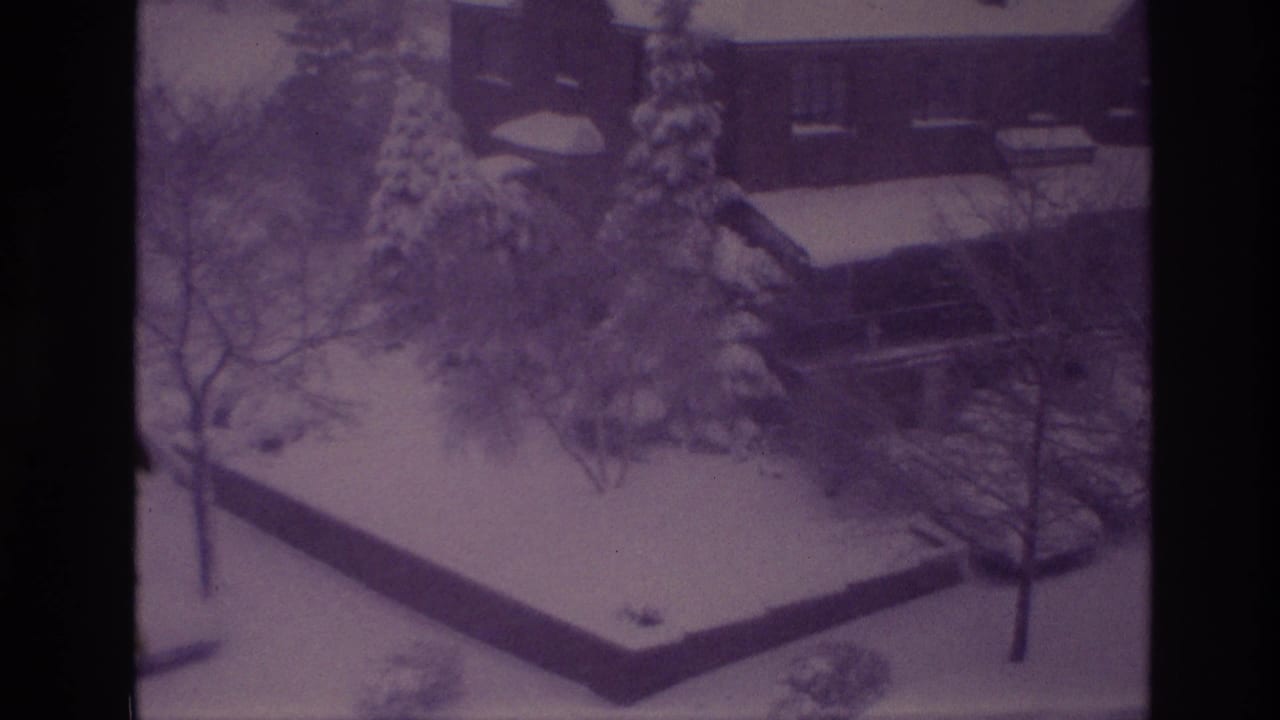 1967 Ottawa home-movie frame showing a snowy residential yard with trees, evergreens, a low wall, and a partially visible house.
