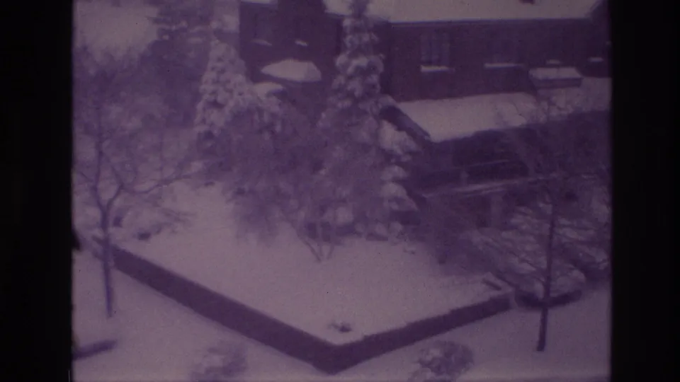 1967 Ottawa home-movie frame showing a snowy residential yard with trees, evergreens, a low wall, and a partially visible house.