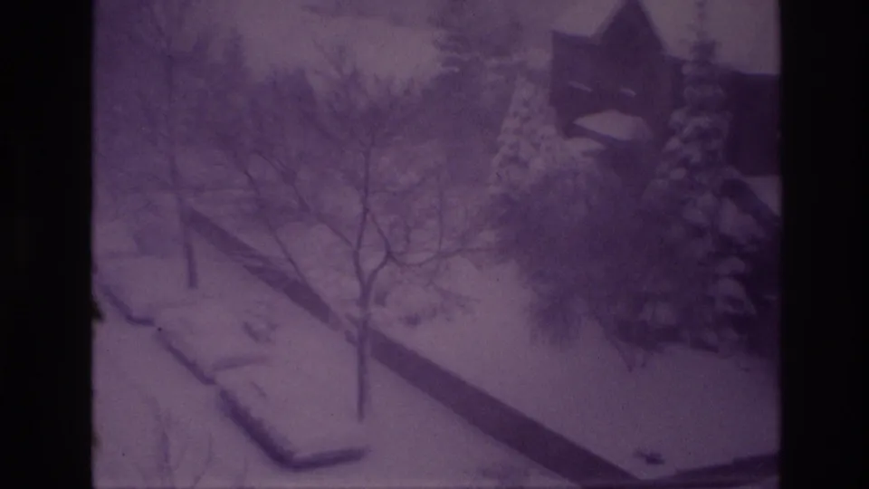 1967 Ottawa frame showing a snow-blanketed residential yard with bare trees, evergreens, a low wall, and part of a nearby building.