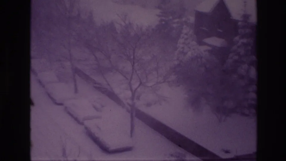 1967 Ottawa home-movie frame of a snowstorm over a quiet residential street, with parked cars and trees partly obscured by falling snow.