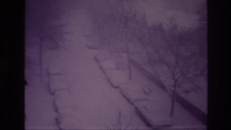 1967 Ottawa home-movie frame showing parked cars largely buried under snow beside a residential road, with bare trees and a purple 8mm cast.