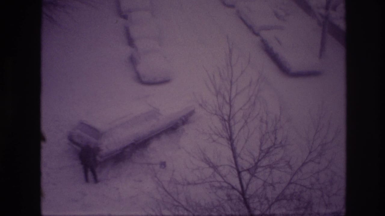 Ottawa 1967 8mm frame showing a distant man clearing snow near a parked car beneath leafless branches.