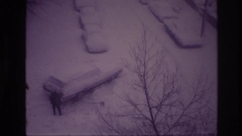 Ottawa 1967 8mm frame showing a distant man clearing snow near a parked car beneath leafless branches.