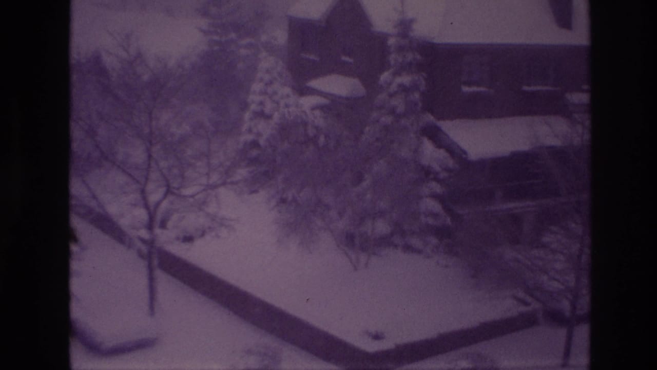 1967 Ottawa home-movie frame widens to a snowy residential area with houses, parked vehicles, leafless trees, and snow-laden evergreens.