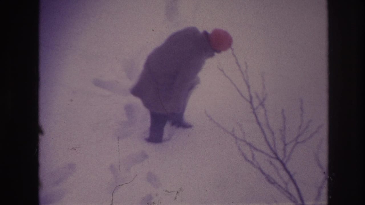 In 1967 Ottawa footage, a bundled person wearing a red hat steps through deep snow near bare foreground branches.