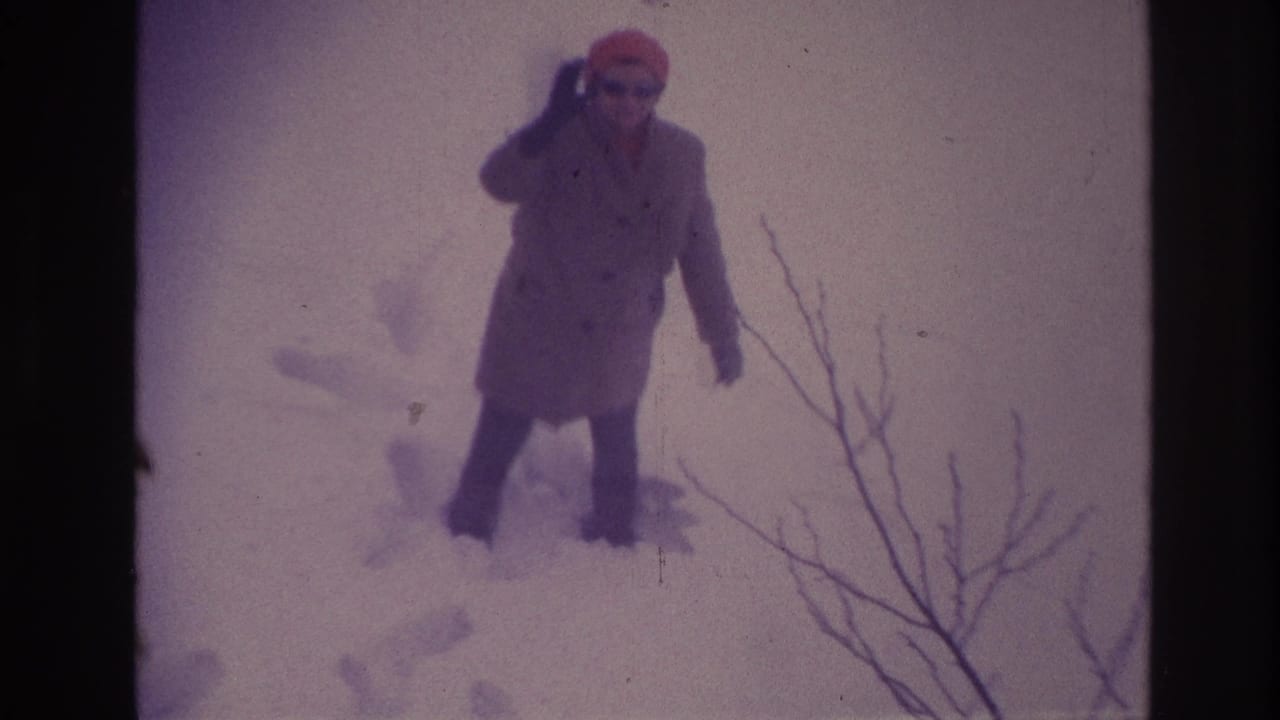 In the 1967 Ottawa home-movie frame, the older woman raises one hand in greeting while standing in deep snow.