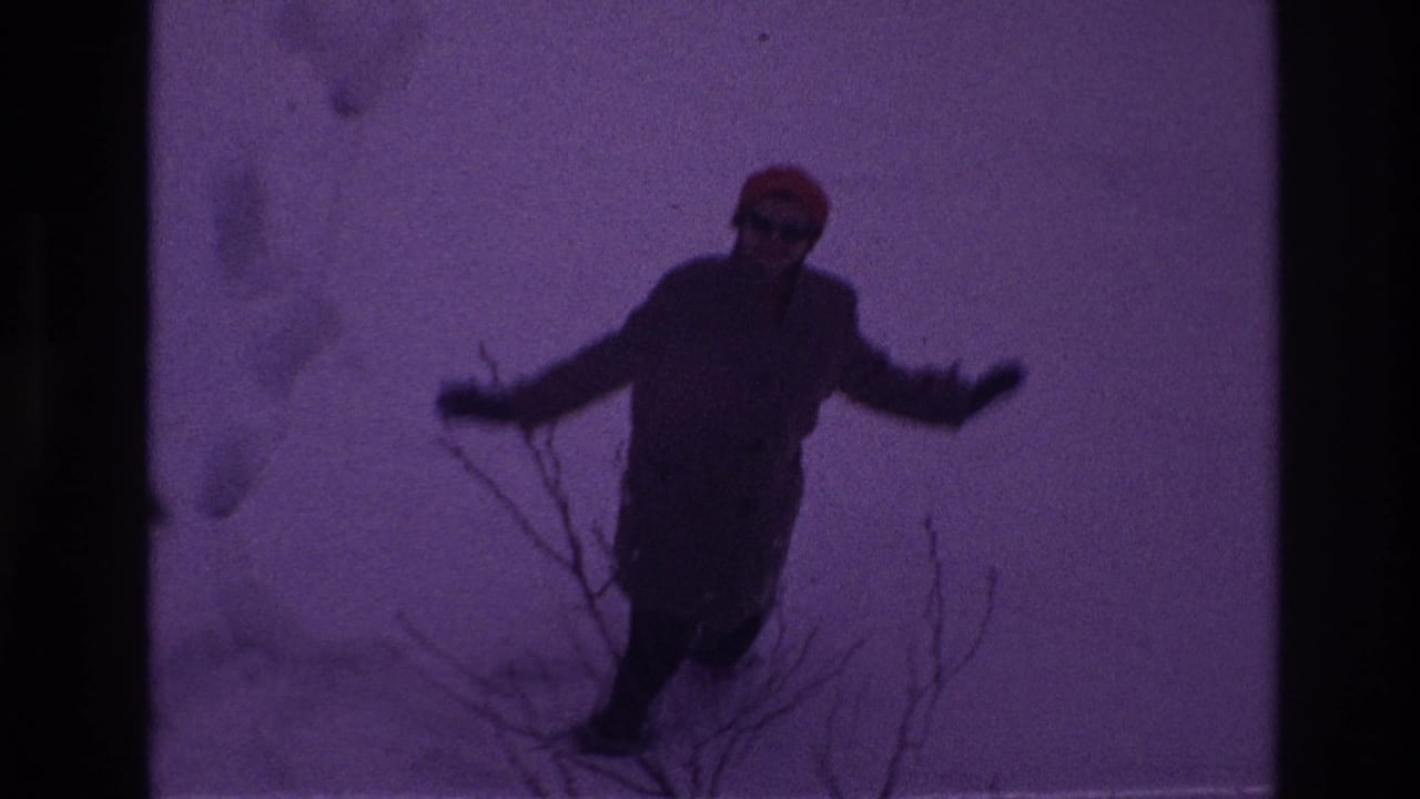 The 1967 Ottawa home-movie frame shows the woman moving through deep snow near bare branches, with a dark purple film cast.