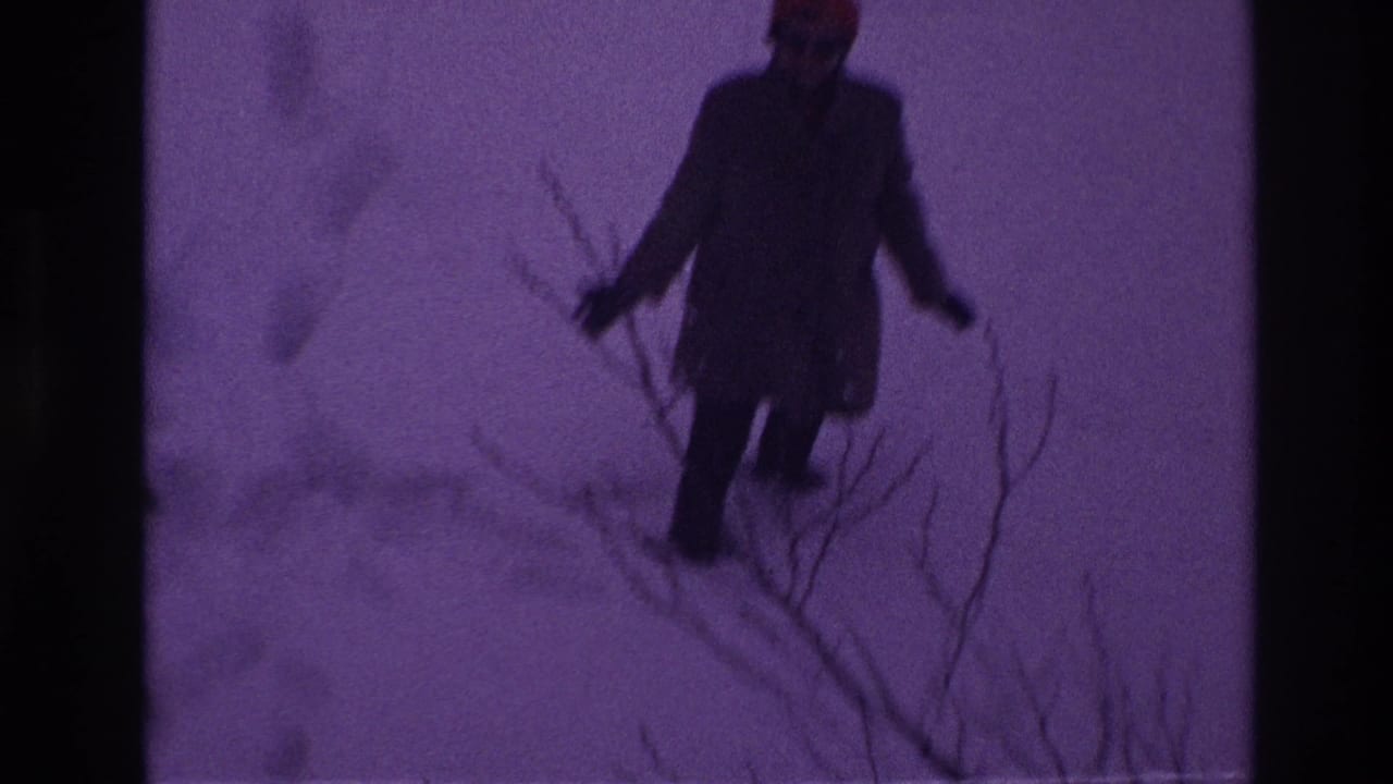 In Ottawa 1967 home-movie footage, a bundled person in a dark coat and red hat walks through deep snow near bare branches.