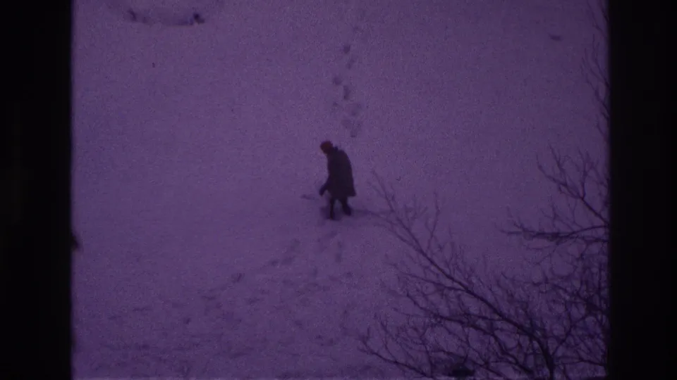 In Ottawa 1967 home-movie footage, a distant man in dark winter clothing walks through deep snow beside bare branches.