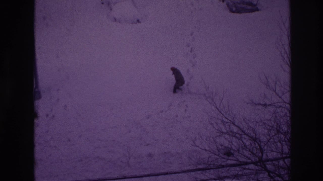 A distant man in dark clothing moves through deep snow in the Ottawa winter yard, seen with strong 8mm color fading.