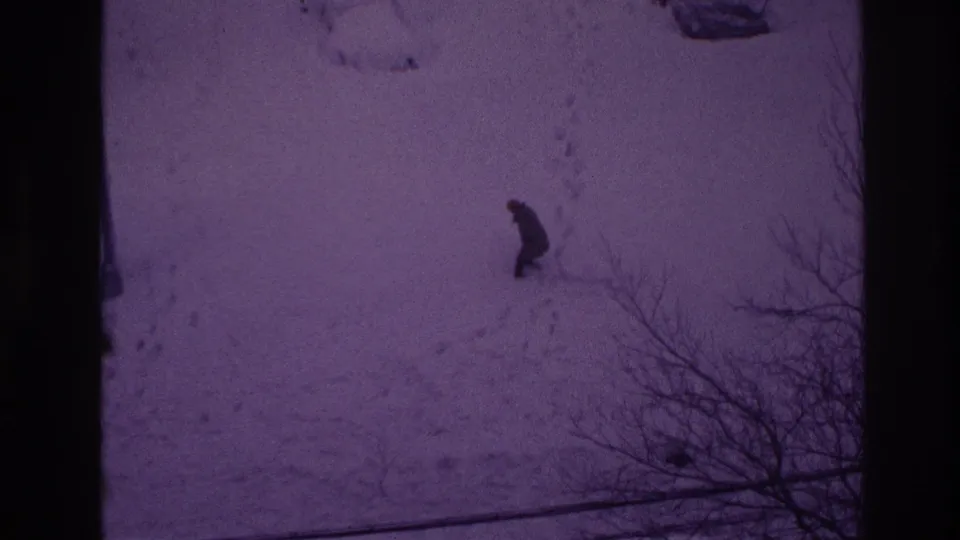 A distant man in dark clothing moves through deep snow in the Ottawa winter yard, seen with strong 8mm color fading.