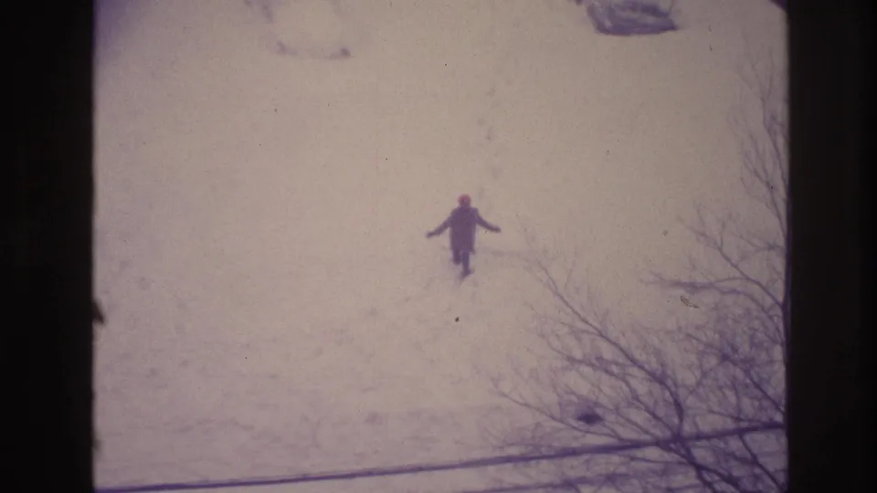 Elevated 1967 Ottawa winter view of a distant figure in a dark coat and red hat raising an arm in the snow.