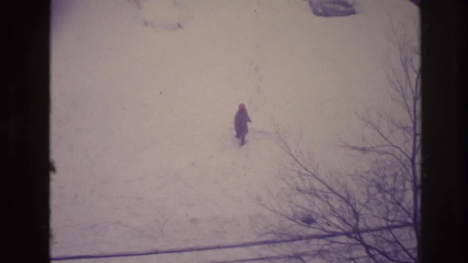 1967 Ottawa home-movie frame of a lone person crossing snowy ground, filmed from above through bare branches.