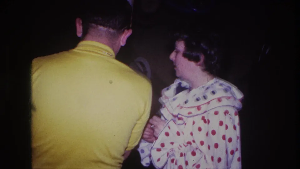 Ottawa 1967 home-movie frame showing a man in a yellow shirt from behind while a costumed woman turns in profile beside him.