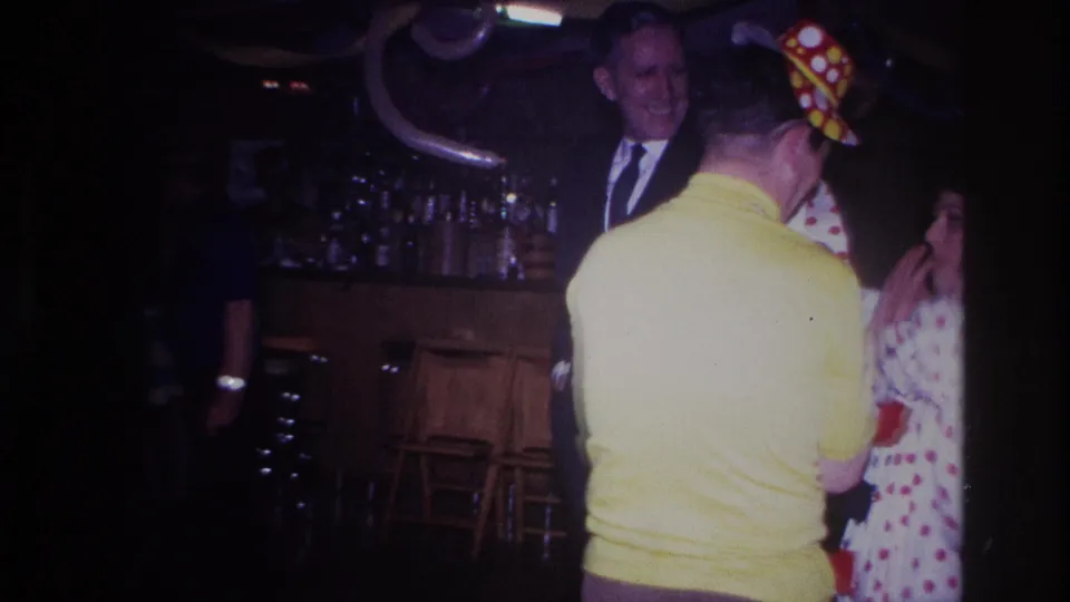 1967 Ottawa party scene with a man in a yellow shirt, a woman in a polka-dot dress, and a suited onlooker beside a decorated bar.