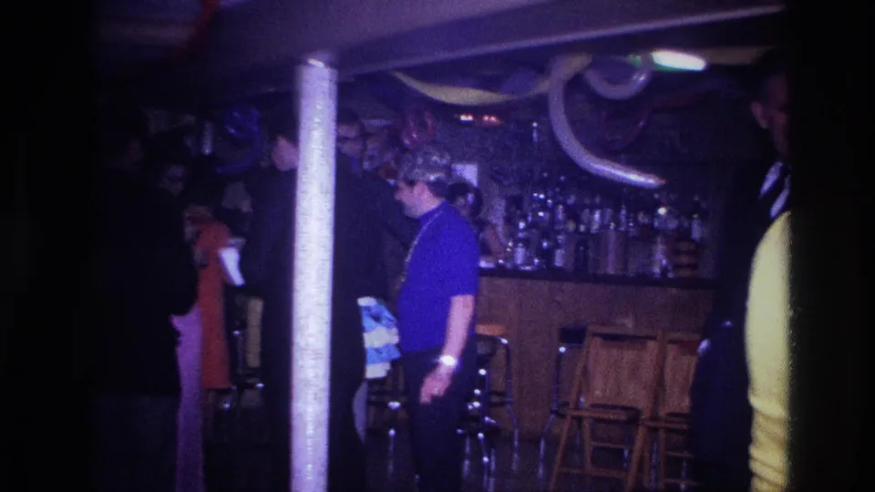 1967 Ottawa home-movie frame showing adults in a dim bar interior with stools, balloons, streamers, and a partially visible party guest.