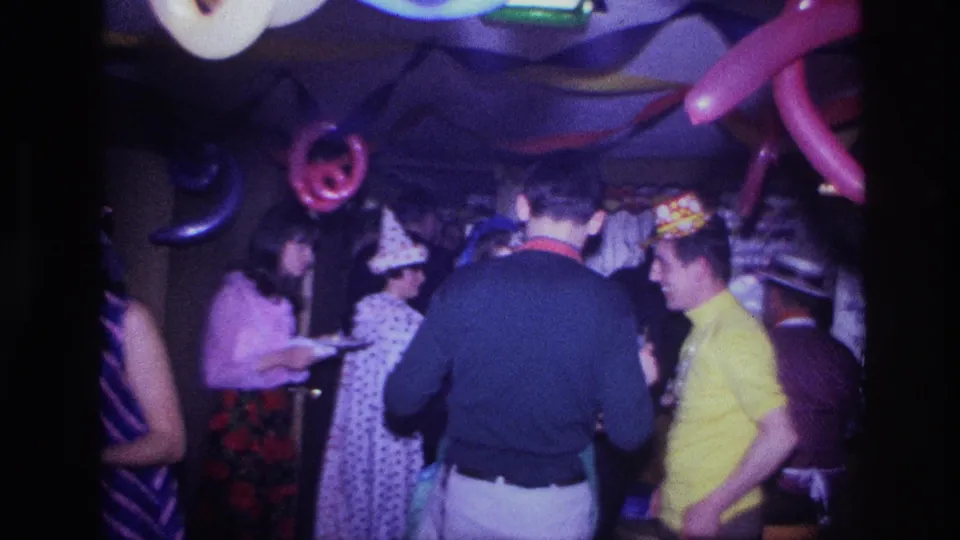 1967 Ottawa party scene with guests conversing near balloon decorations, including a person in a party hat and a man in a yellow shirt.
