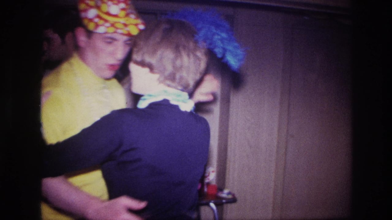 Costumed couple dancing indoors beside a staircase in dim 8mm footage.