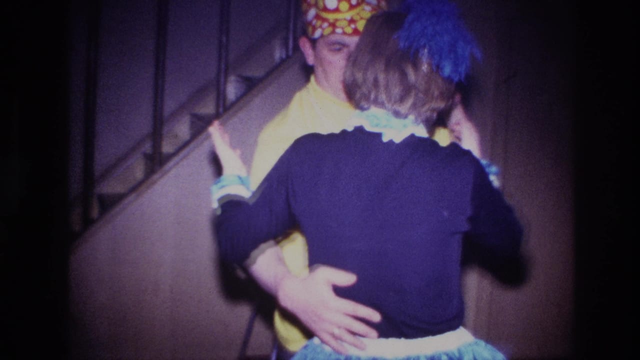 Man in yellow costume holds a woman as they dance near stairs.