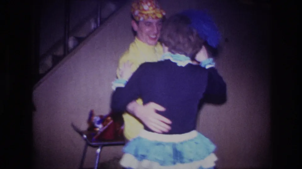 The man smiles while holding his dance partner in a dim Ottawa interior, captured on 8mm home-movie film in 1967.