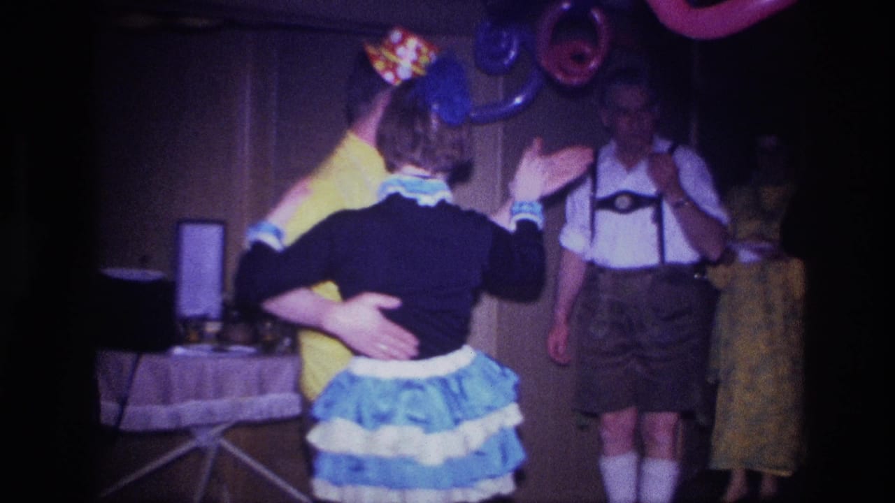 Dancing couple turns in front of balloons while costumed guests stand nearby.